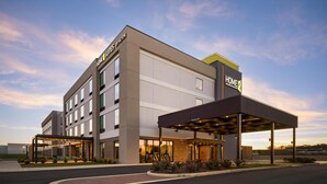 A hotel with a covered outdoor seating area, a parking lot, and a clear sky. - Home2 Suites By Hilton Calera (Calera)