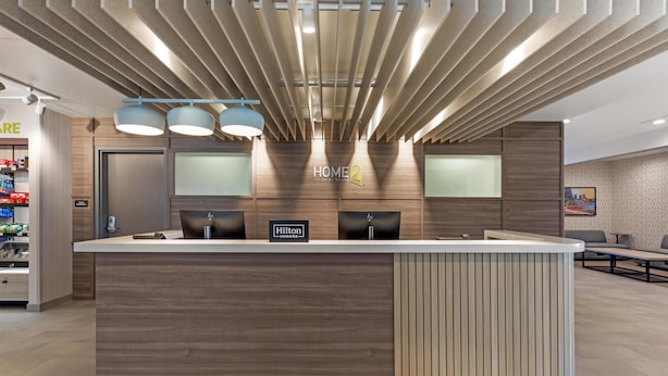 A modern hotel reception desk with a wooden finish, a 'Hilton Honors' sign, and a 'Home2' logo. - Home2 Suites By Hilton Calera (Calera)