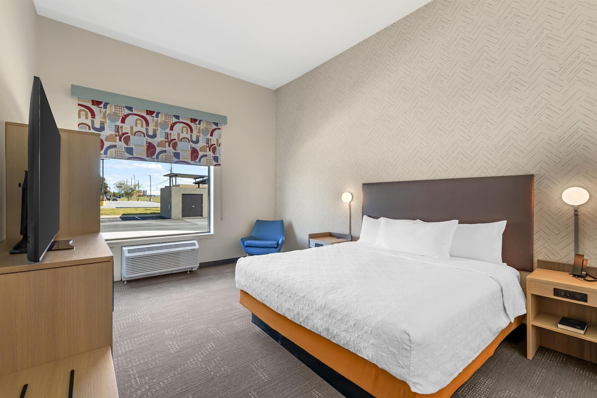 A hotel room with a bed, a television, a chair, a desk, and a window with a view.