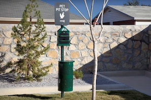 A pet waste station with a sign, a green trash bin, and a stone wall in the background. - Home2 Suites By Hilton El Paso East Loop 375 (El Paso)