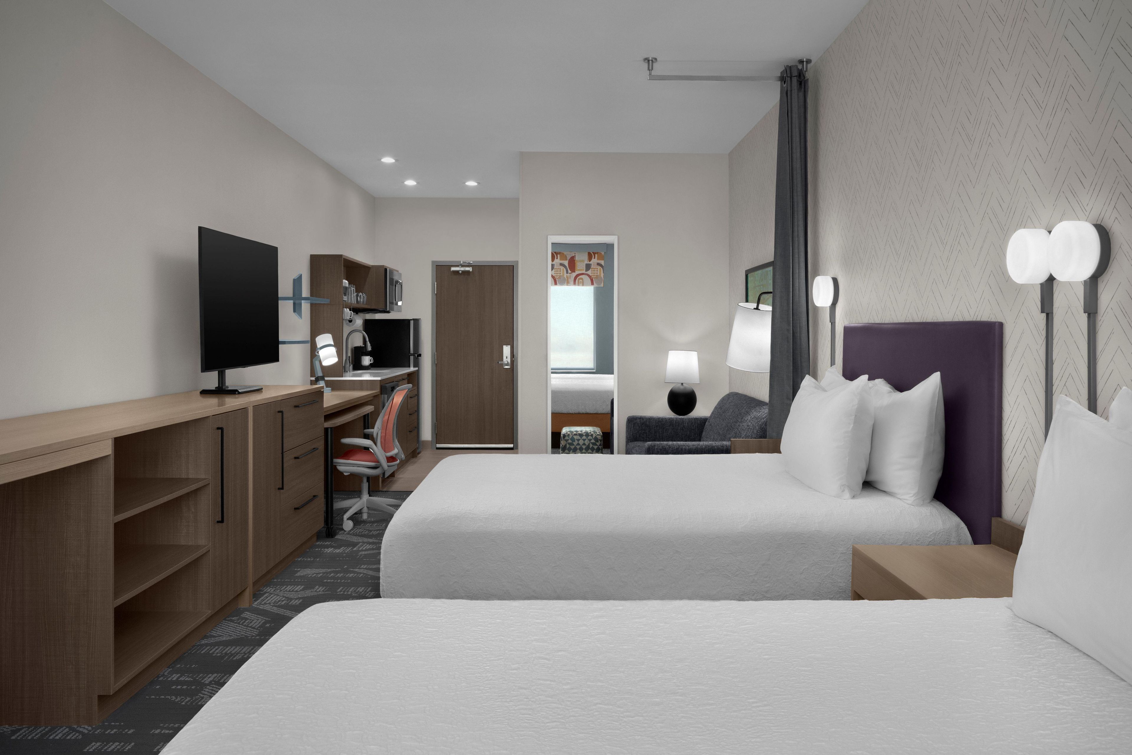 A hotel room with a bed, desk, television, and a bathroom door.
