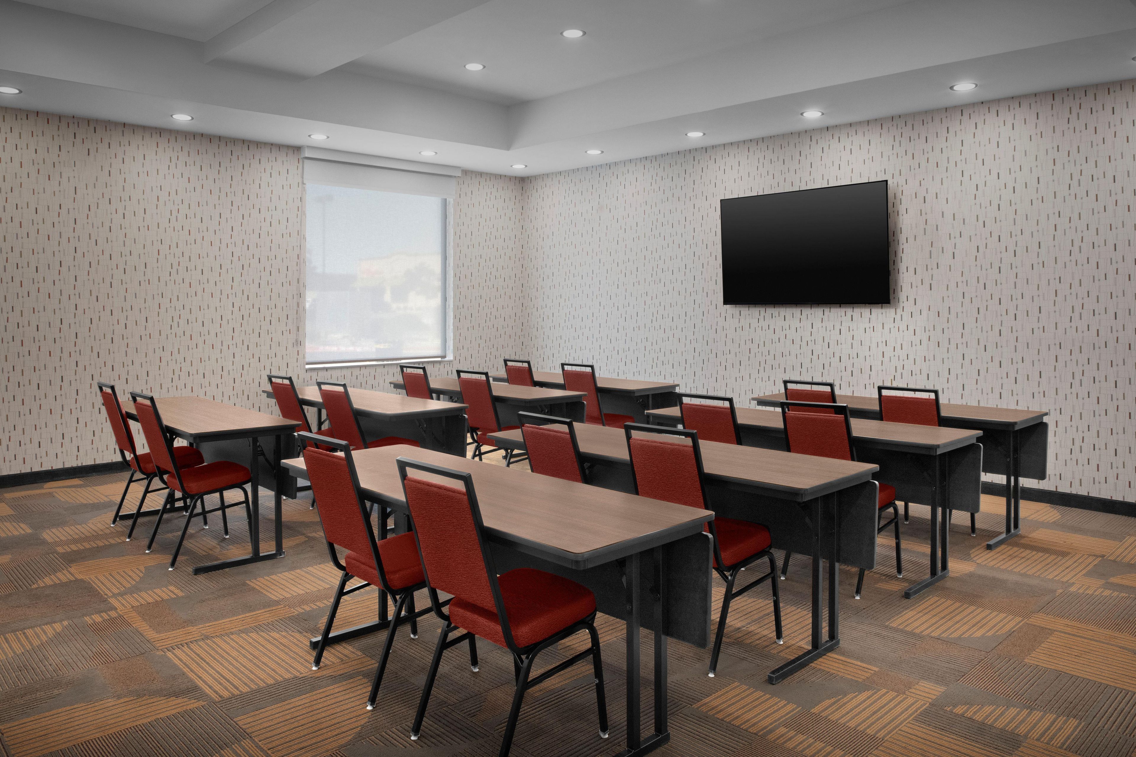 A conference room with multiple tables and chairs, a large window, and a flat-screen TV mounted on the wall.