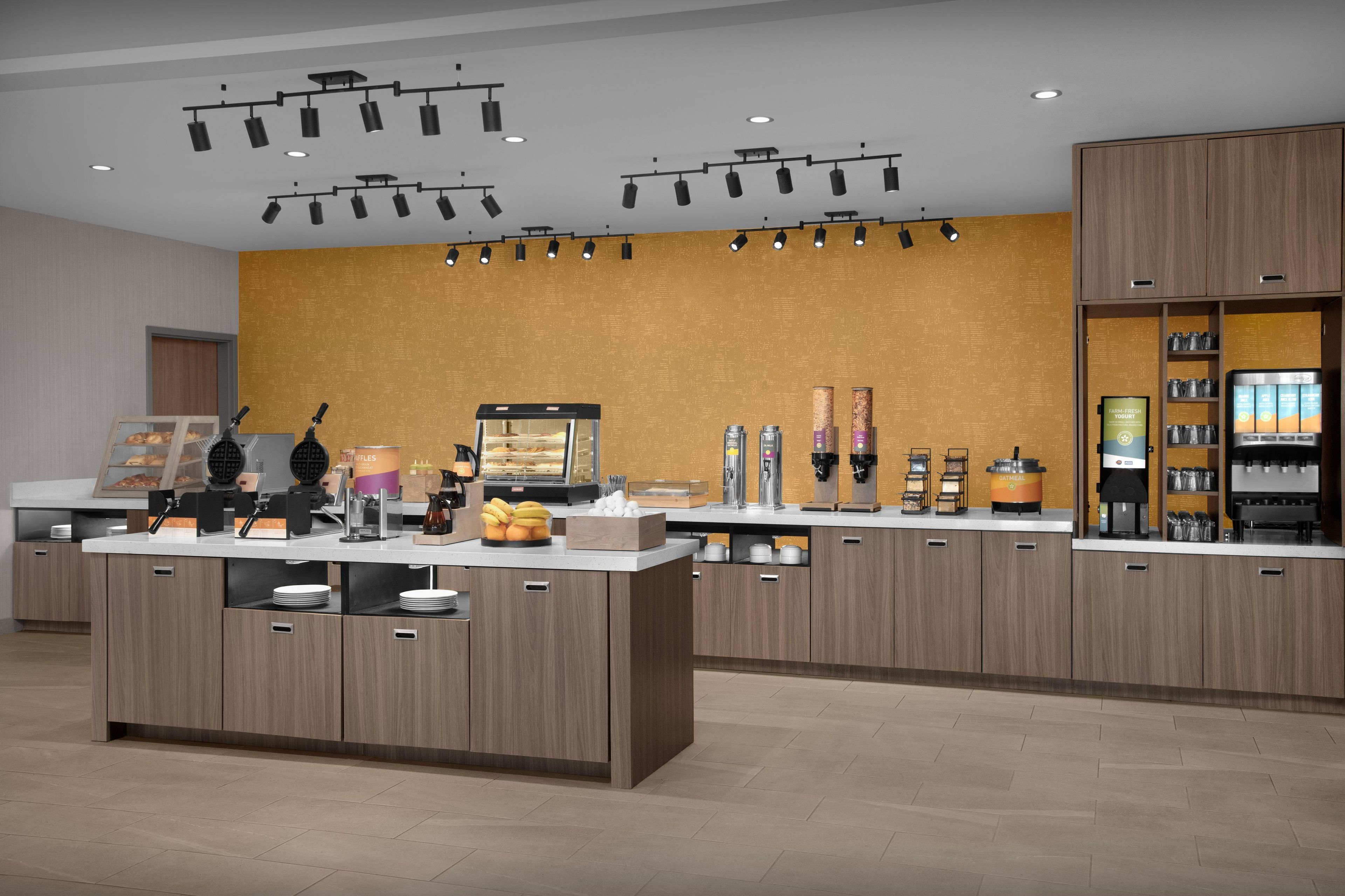 A modern kitchen area with a central island, overhead lighting, and a variety of appliances and food items.