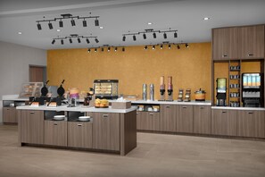 A modern kitchen area with a central island, overhead lighting, and a variety of appliances and food items. - Home2 Suites By Hilton El Paso East Loop 375 (El Paso)
