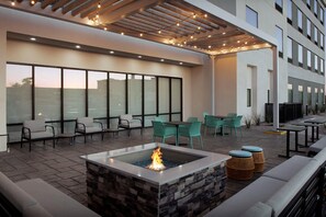 Un patio exterior moderno con un brasero, asientos y ventanas amplias.