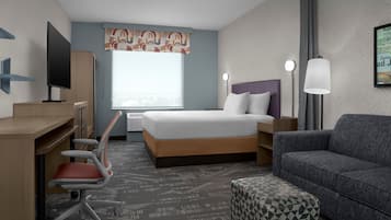 Una habitación de hotel con cama, escritorio, silla, sofá y un otoman estampado.