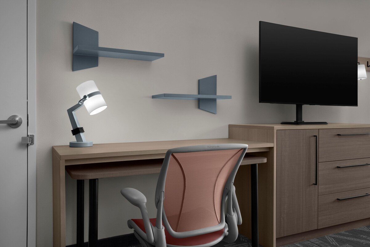 A modern office space with a desk, chair, TV, and wall-mounted shelves.
