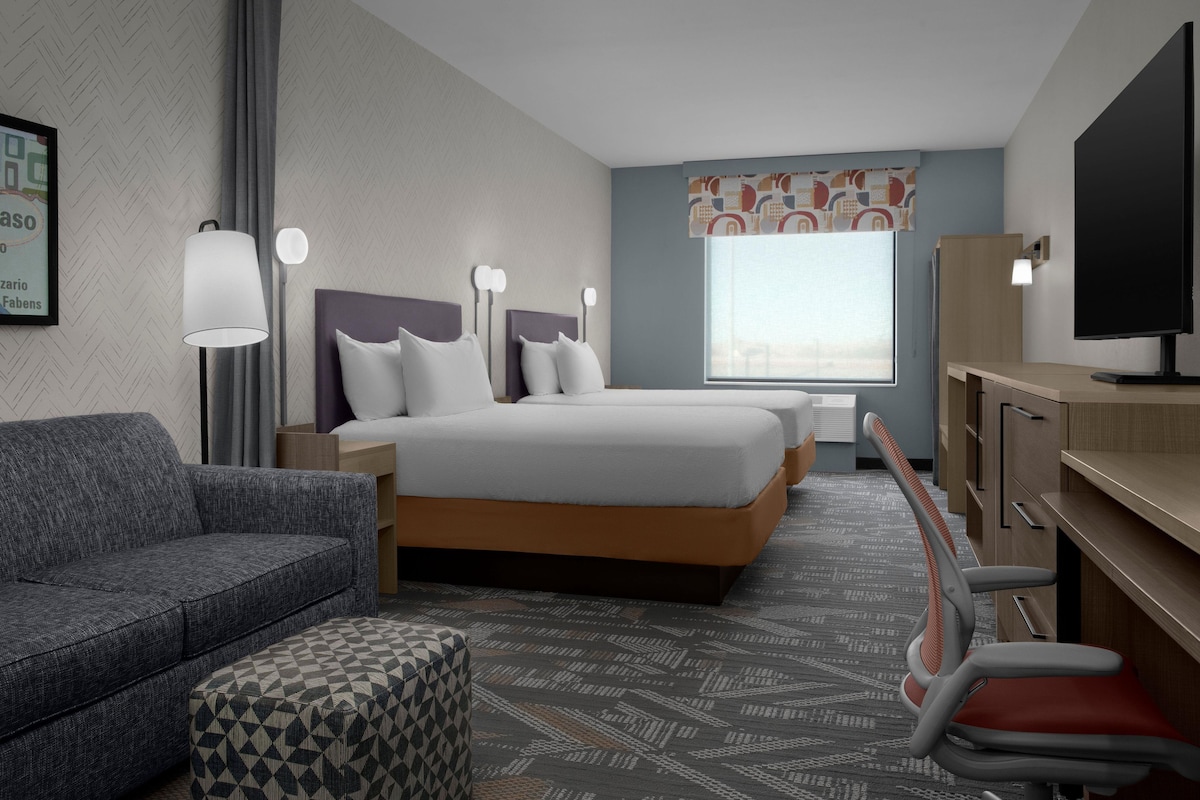 A hotel room with a bed, a sofa, a desk, a chair, and a television.