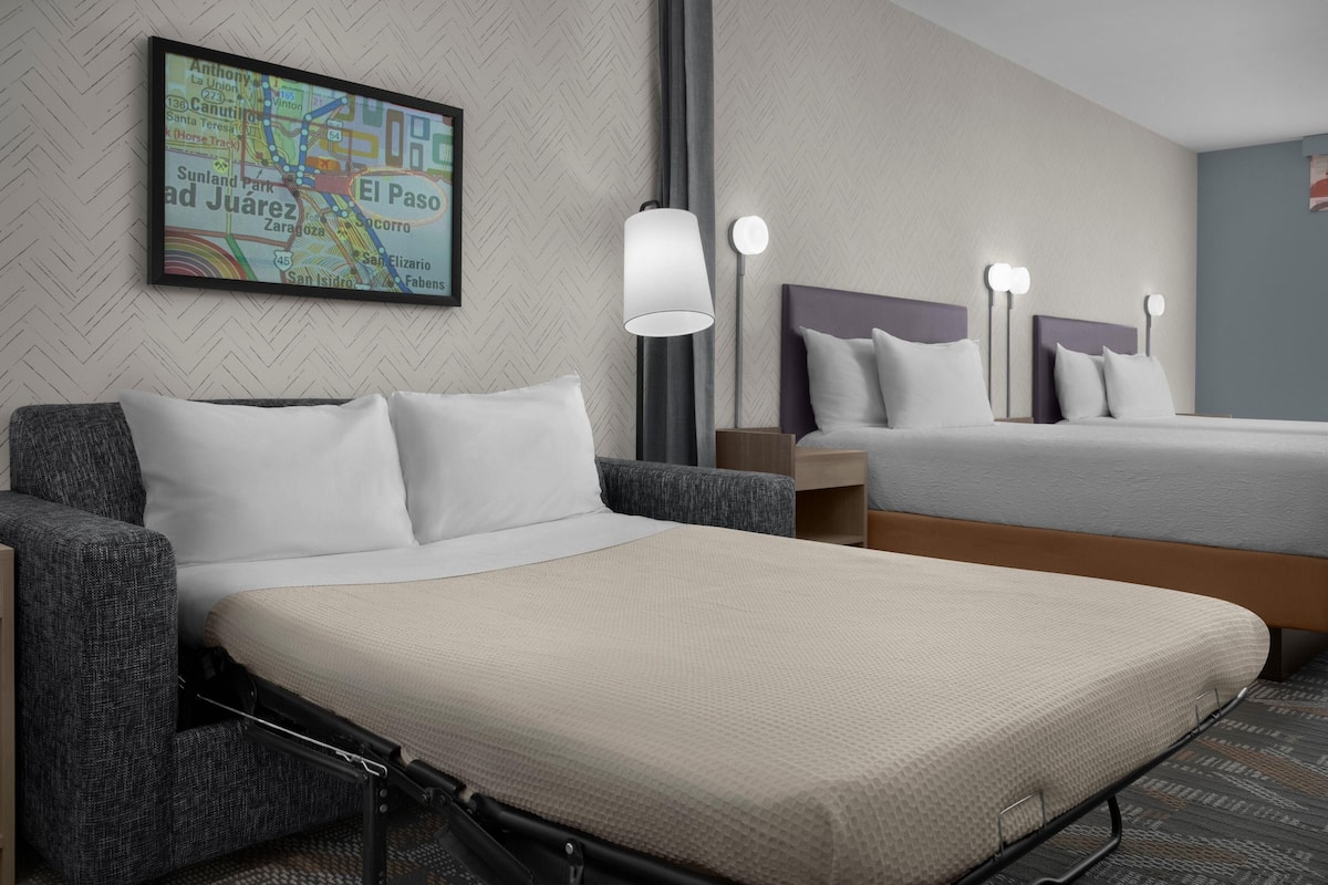 Ein Hotelzimmer mit einem Bett, einem Sessel, einer Karte an der Wand und einer Lampe.