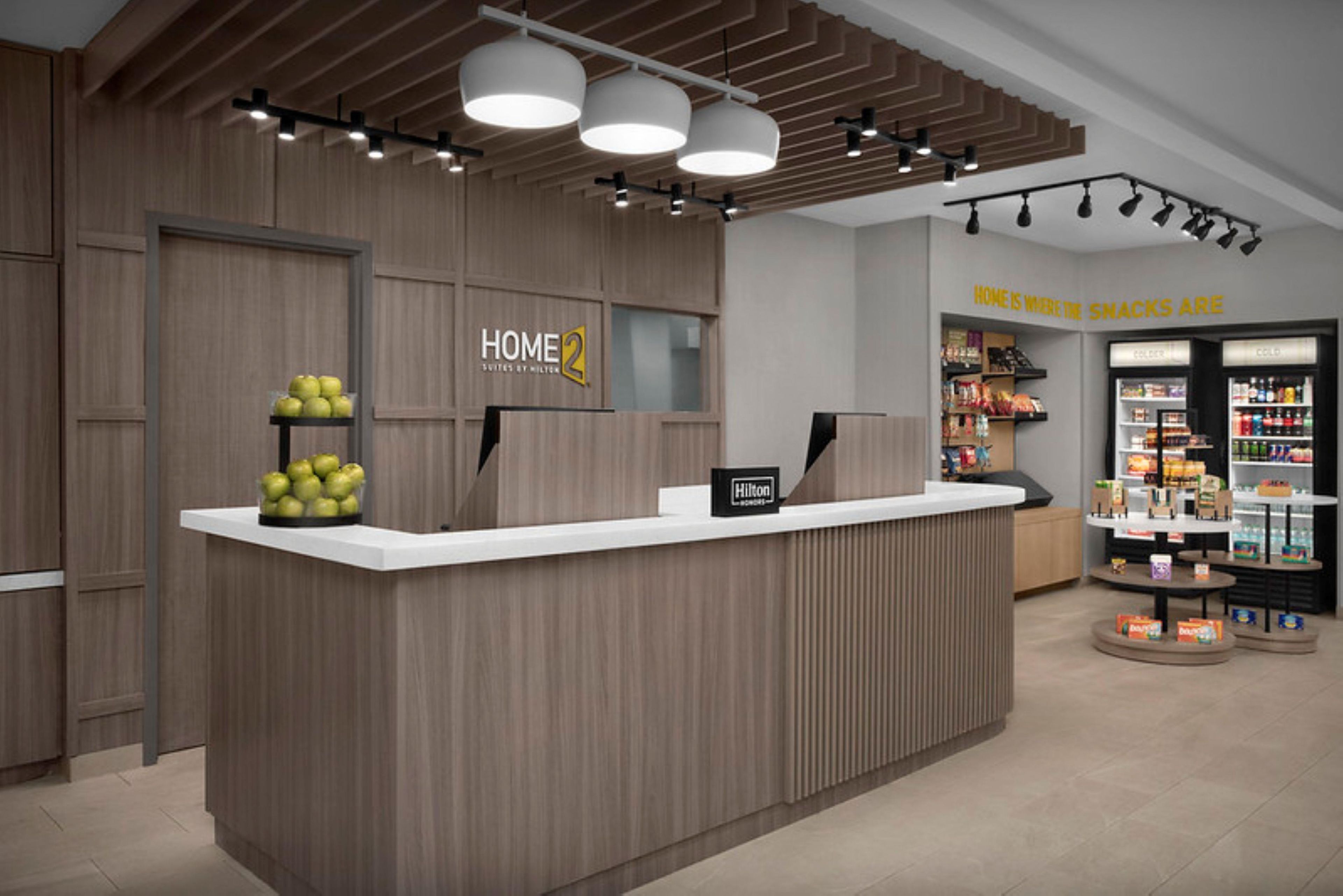 A reception desk with a wooden finish, a sign reading 'HOME 2 Suites by Hilton,' and a 'Hilton' sign on the wall.