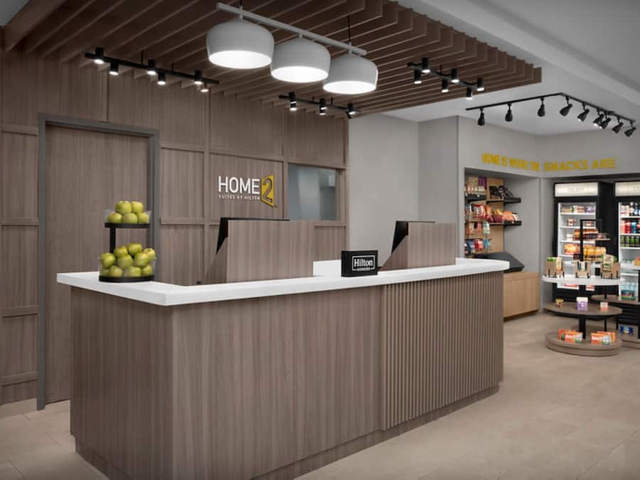 A reception desk with a wooden finish, a sign reading 'HOME 2 Suites by Hilton,' and a 'Hilton' sign on the wall.
