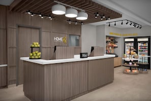 Een receptiebalie met een houten afwerking, een bord met de tekst 'HOME 2 Suites by Hilton', en een 'Hilton' bord aan de muur.