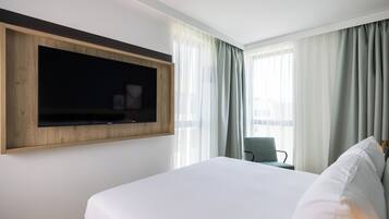 Une chambre d’hôtel avec un grand lit, un téléviseur fixé au mur, une chaise et une fenêtre avec des rideaux.