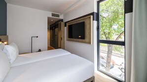 Habitación de hotel con cama, televisor montado en la pared y ventana con vista a la calle.