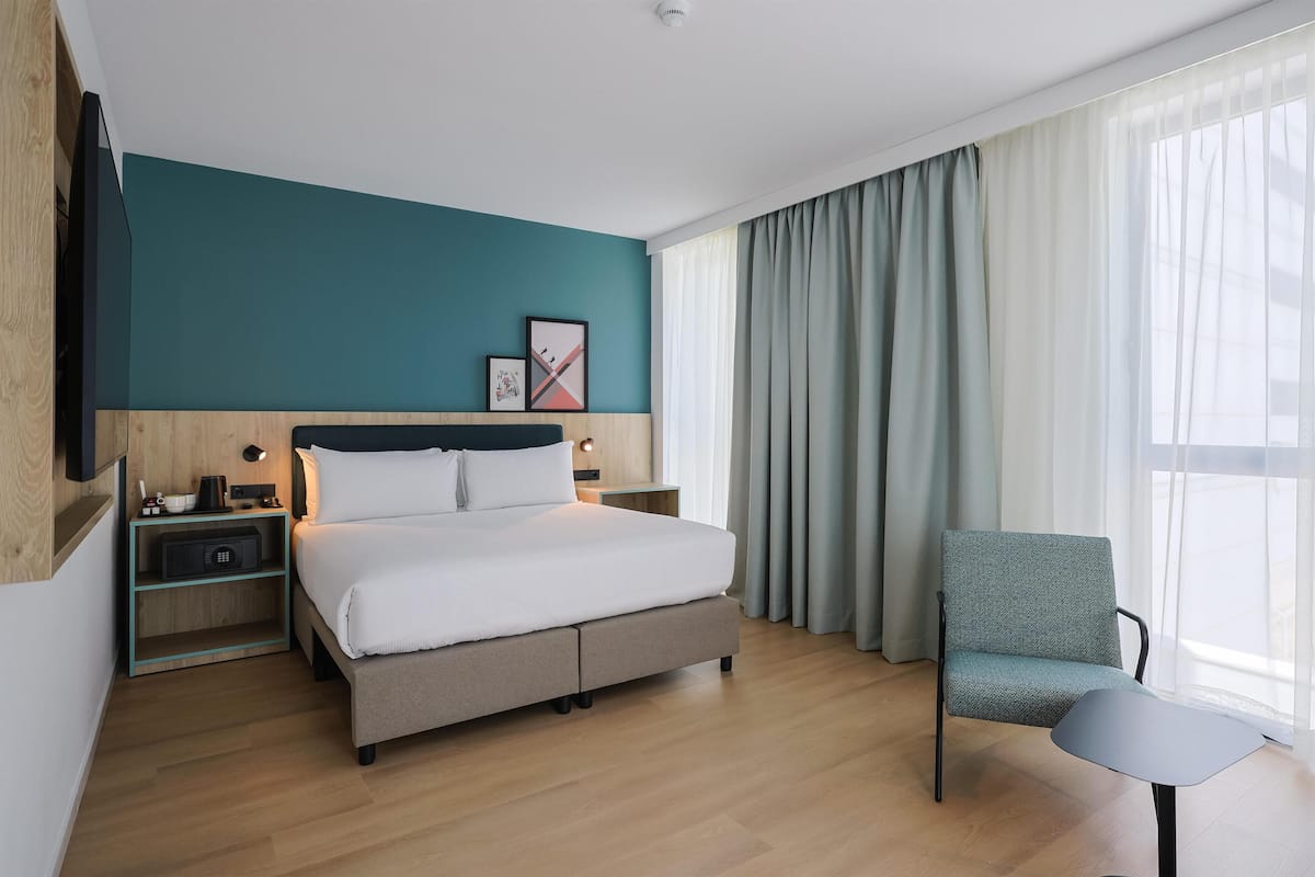 Una habitación de hotel moderna con cama, una silla, una mesita de noche y un televisor instalado en la pared.