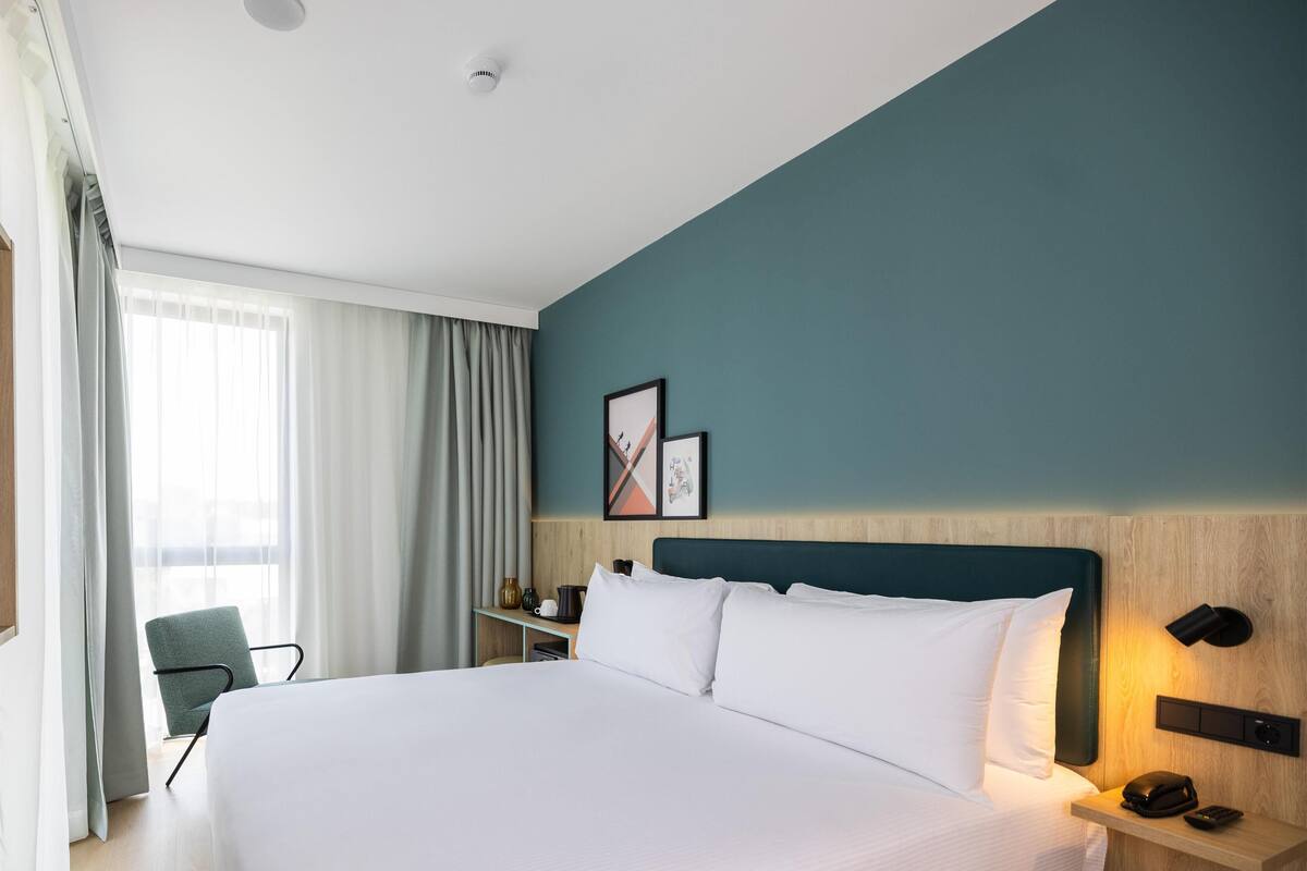 Una habitación de hotel con una cama grande, un escritorio con lámpara, una silla y una ventana con cortinas.