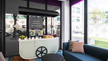 A modern living room with a retro-style kitchenette, a sofa, and a large window offering a view of the street.