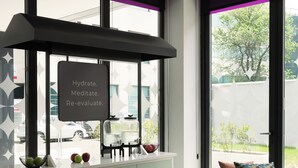 Un interior moderno con una encimera blanca, un extractor negro y un letrero que dice 'Hydrate. Meditate. Re-evaluate'. Hay sillas, una mesa redonda y un sofá con cojines.