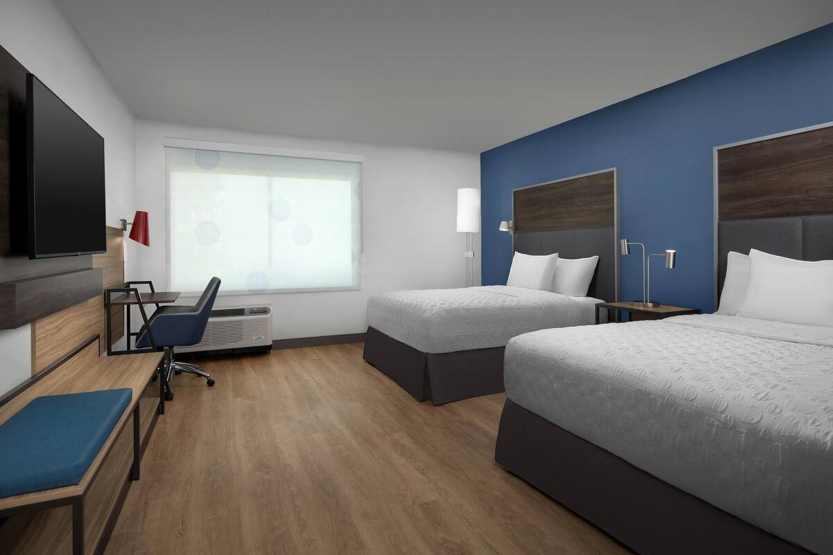 Habitación de hotel con dos camas, un escritorio, una silla, un televisor y una ventana con persianas.
