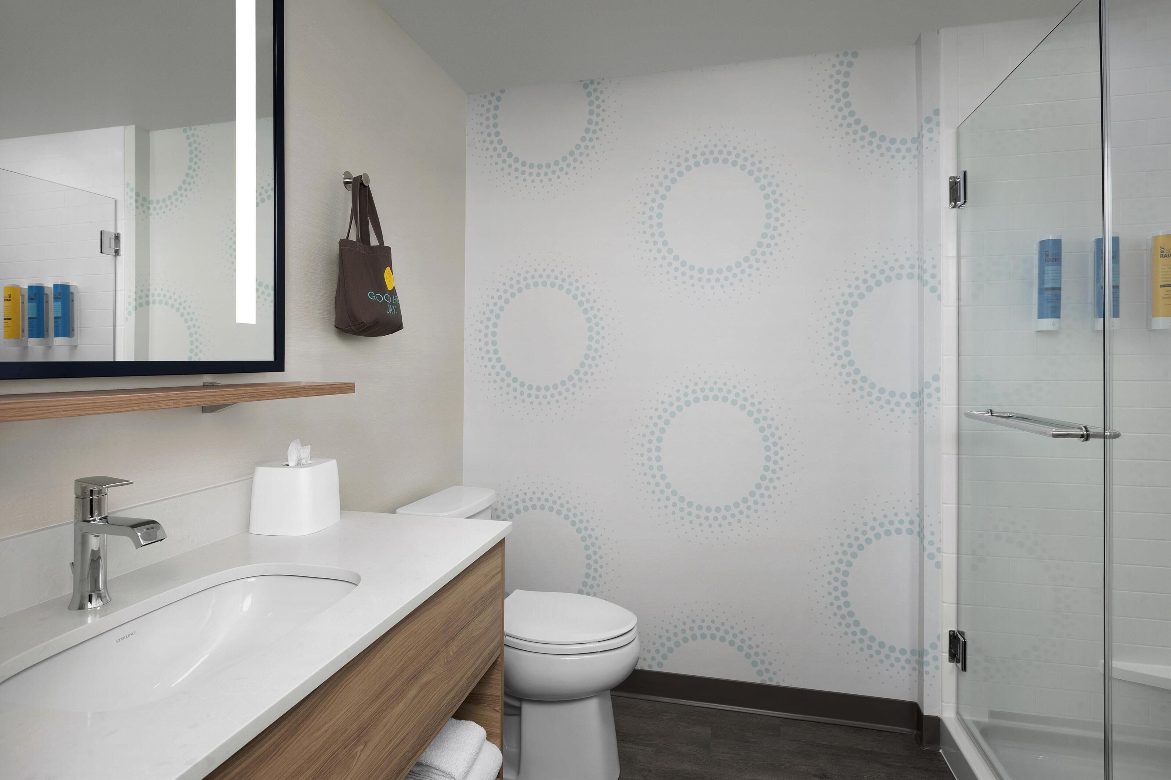 A modern bathroom with a white sink, a mirror, a toilet, and a glass shower enclosure.