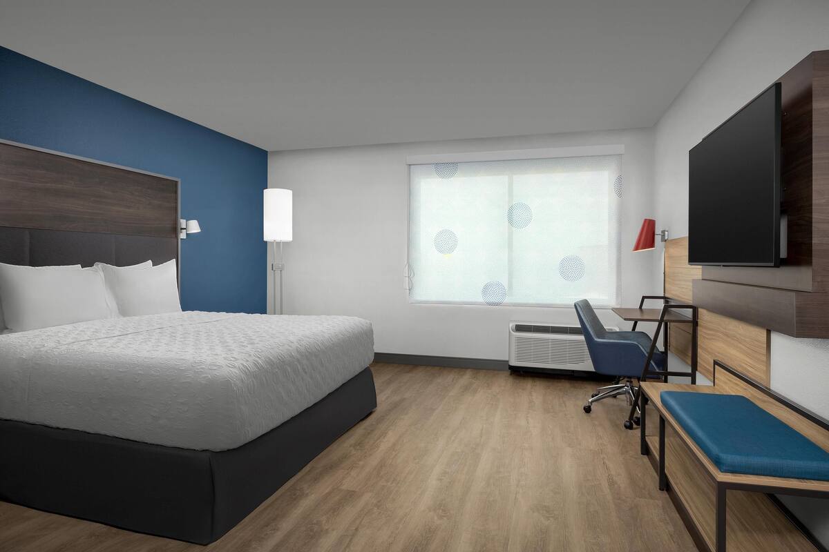 Una habitación de hotel moderna con una cama grande, un escritorio, una silla, un televisor y una ventana con persianas.