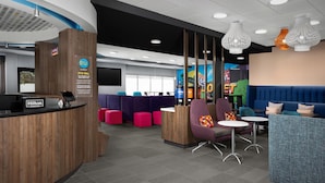 A modern hotel lobby with a wooden reception desk, seating areas, and a mural of a highway. - Tru By Hilton Joliet Plainfield (Joliet)