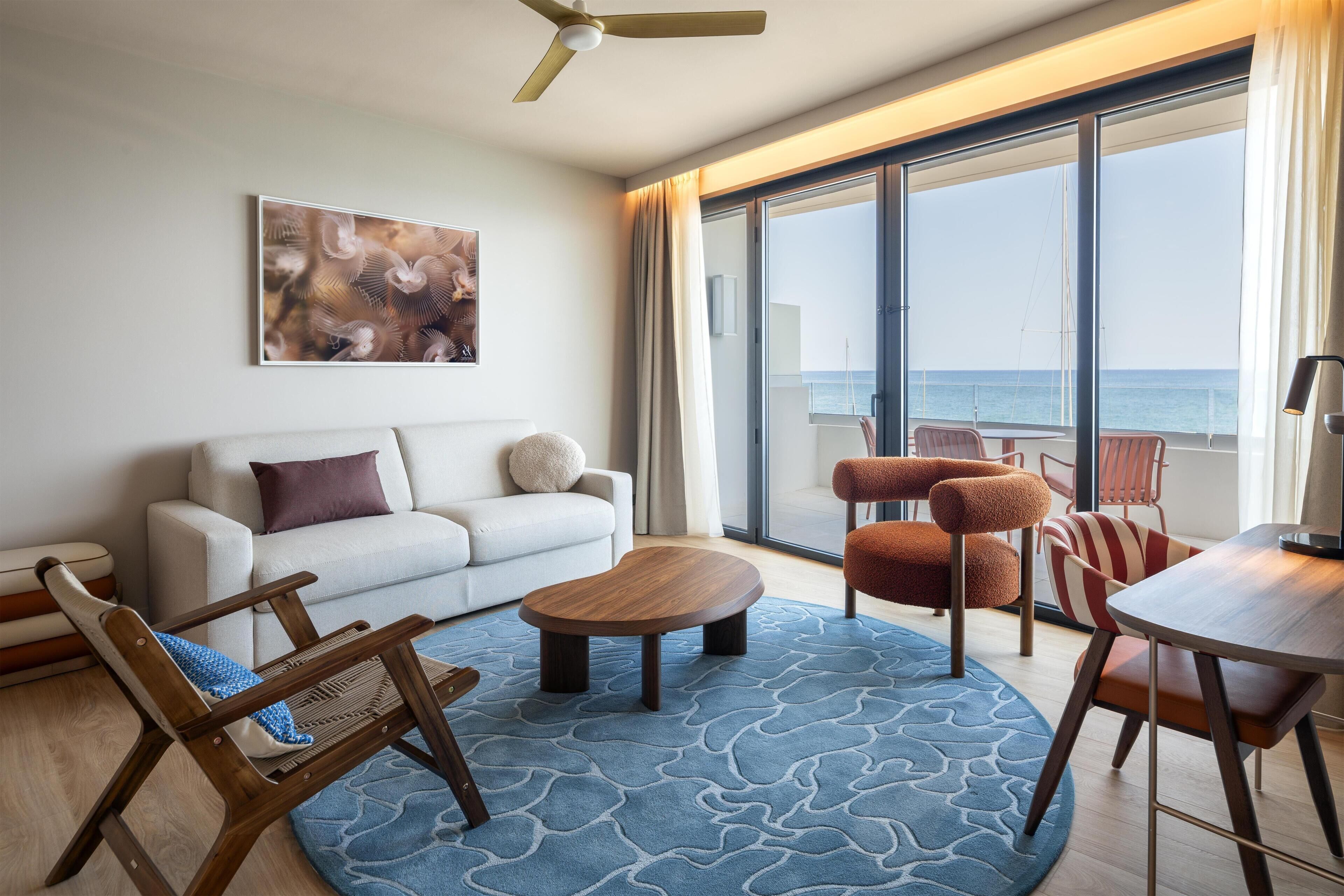 Un salon moderne avec un canapé, une table basse et une vue sur la mer grâce à de grandes fenêtres.