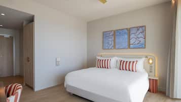 Quarto de hotel moderno com uma cama grande, um ventilador de teto, uma mesa de cabeceira com abajur e arte abstrata na parede.