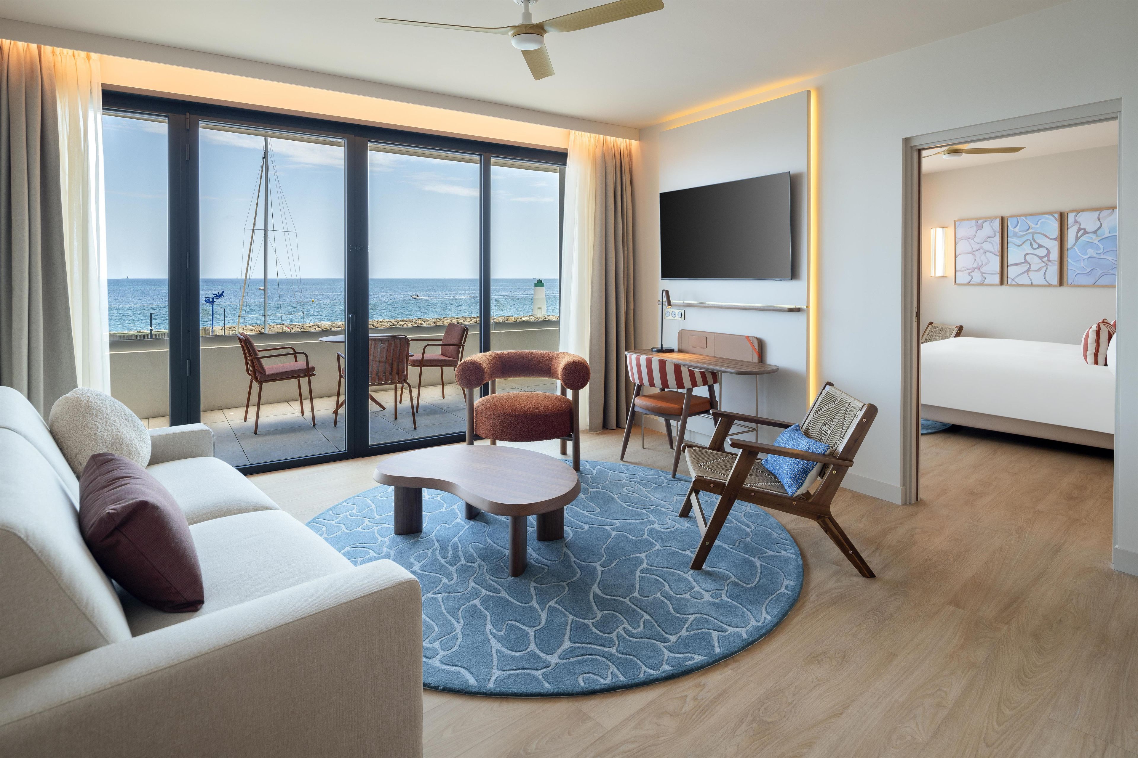 A hotel room with a large balcony, a sofa, a coffee table, and a bed.