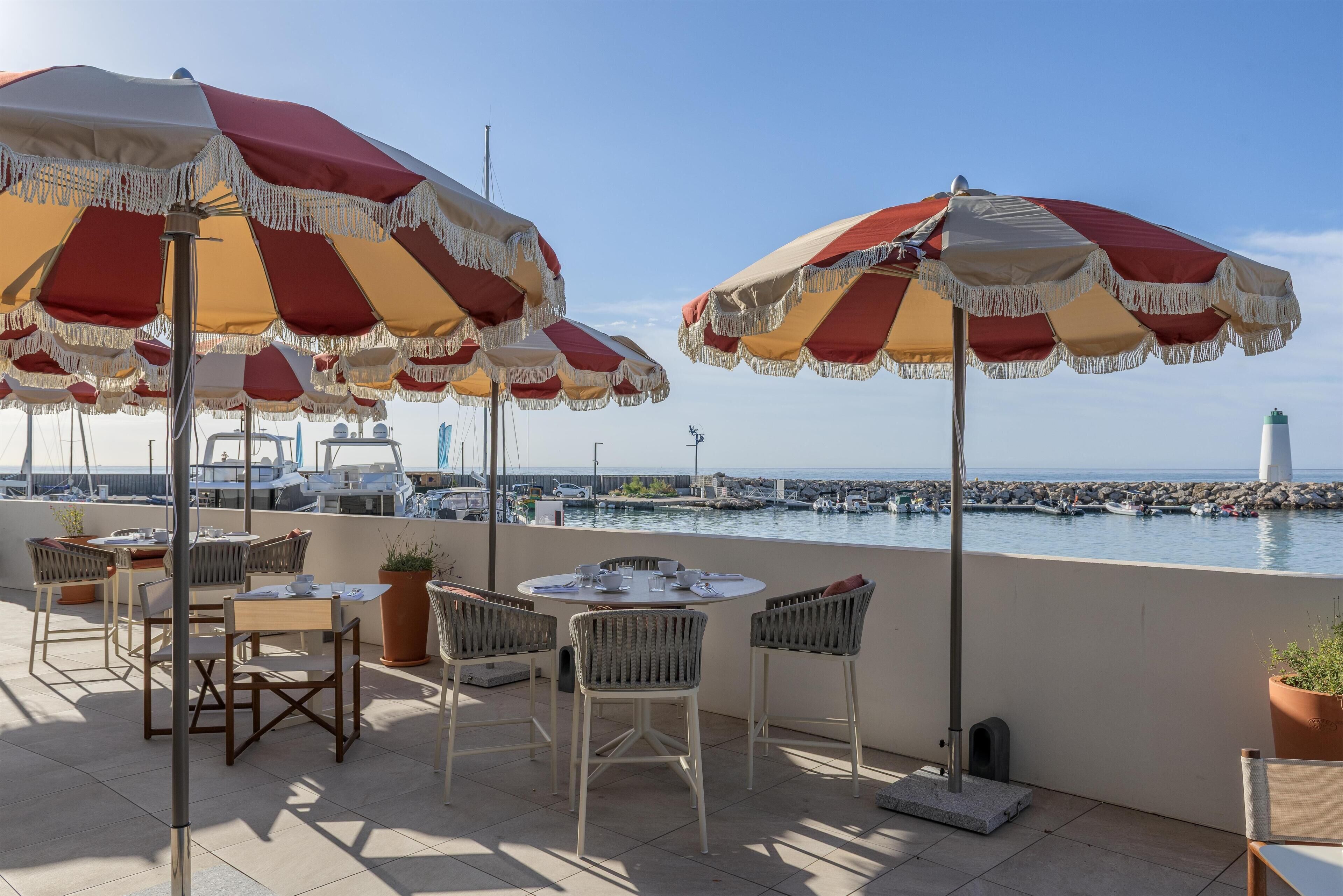 Une terrasse avec des places assises à l’extérieur, une vue sur la mer et un phare visible au loin.