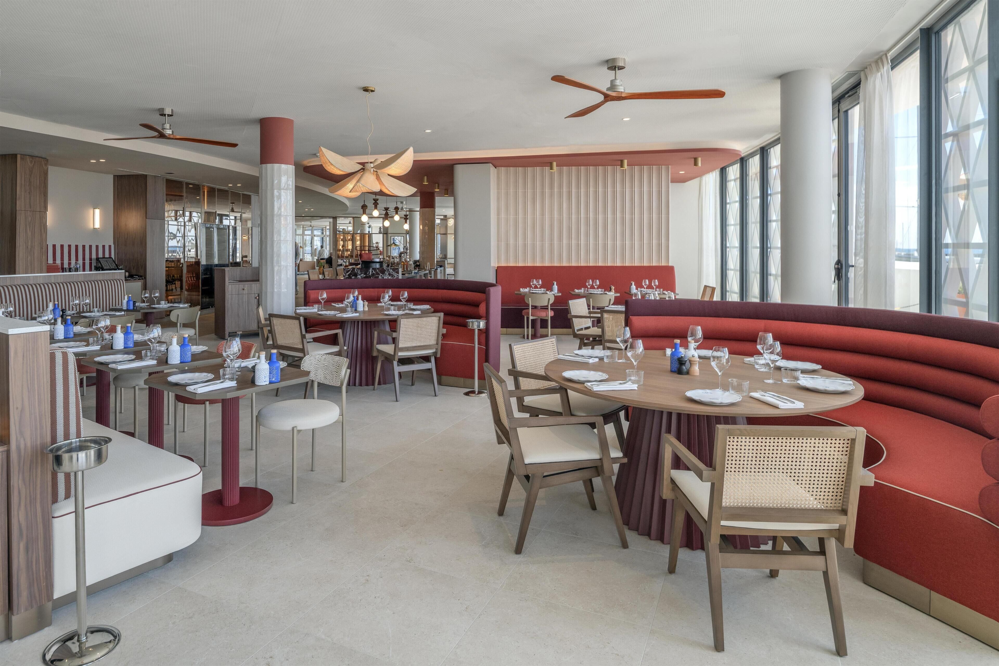 Een restaurant met ronde tafels, rode banken en een bar.