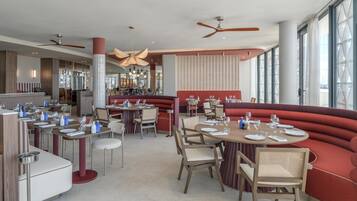 Een restaurant met ronde tafels, rode banken en een bar.