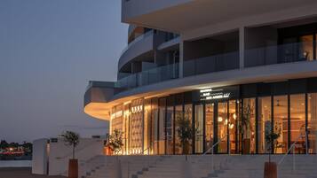 A modern hotel with a curved facade, multiple balconies, and a staircase leading to the entrance.