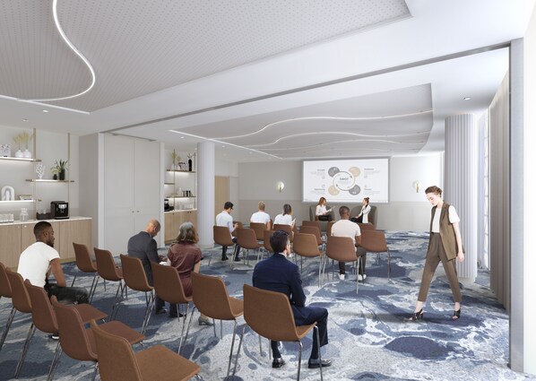 A modern conference room with a presentation screen, seated attendees, and a speaker. - Marina Baie des Anges Hotel, Curio Collection by Hilton (Villeneuve-Loubet)