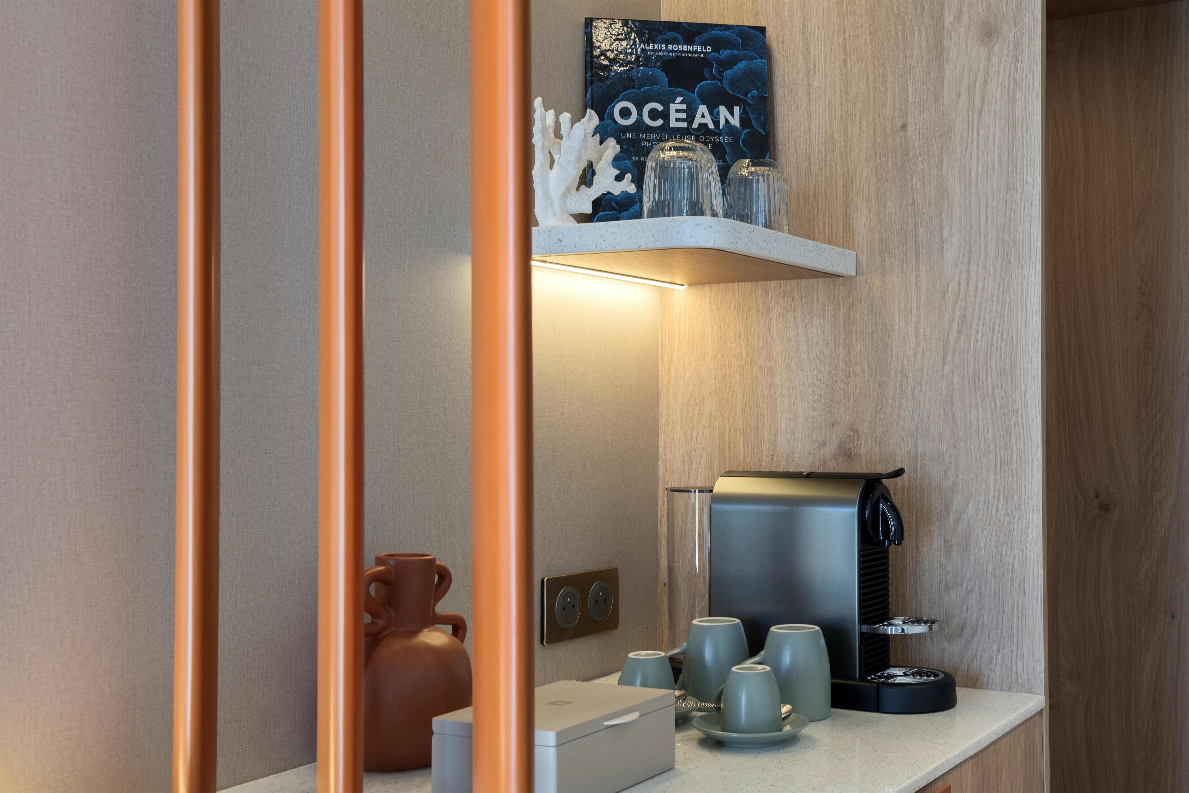 Een keukenhoek met een koffiezetapparaat, bekers en een boek met de titel 'OCEAN' op een plank.