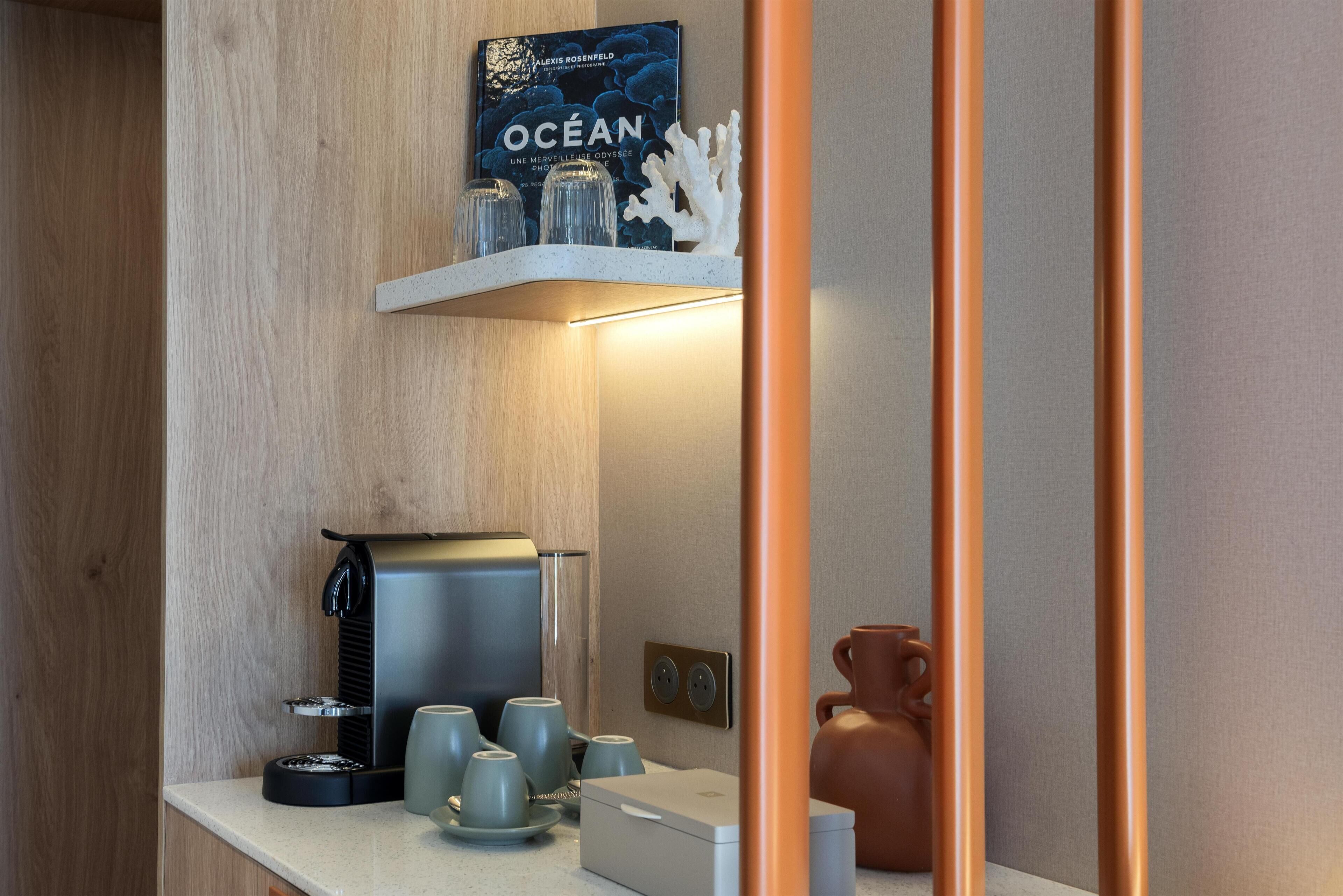 A modern kitchen with a coffee machine, cups, and a book titled 'OCEAN' on the counter.