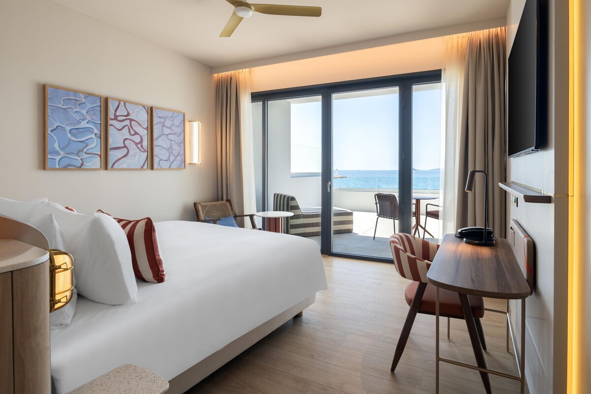 Una habitación de hotel con cama, escritorio, silla, televisor y vista al mar.