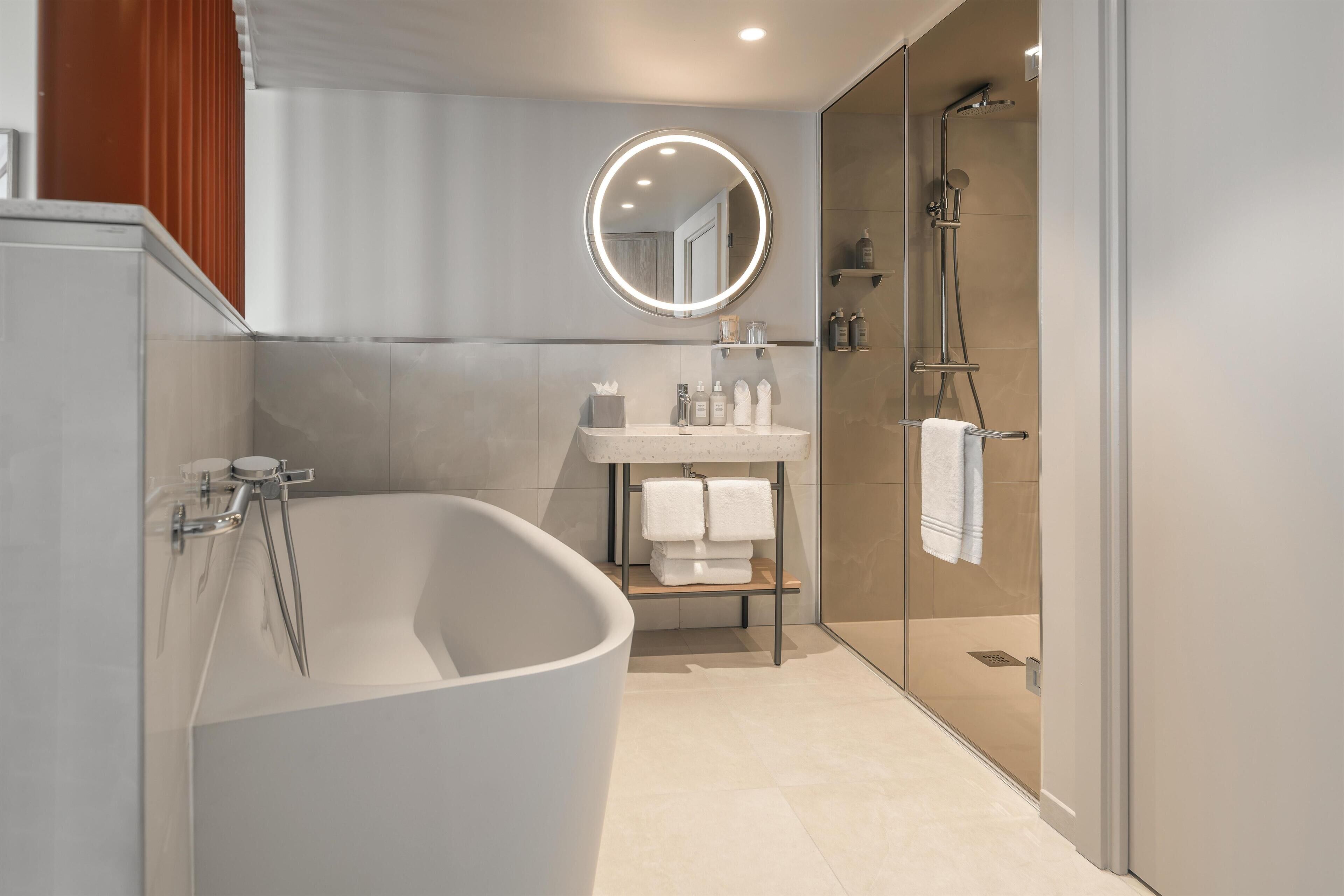 Ein modernes Badezimmer mit freistehender Badewanne, einer gläsernen Duschkabine und einem Waschtisch mit Spiegel.