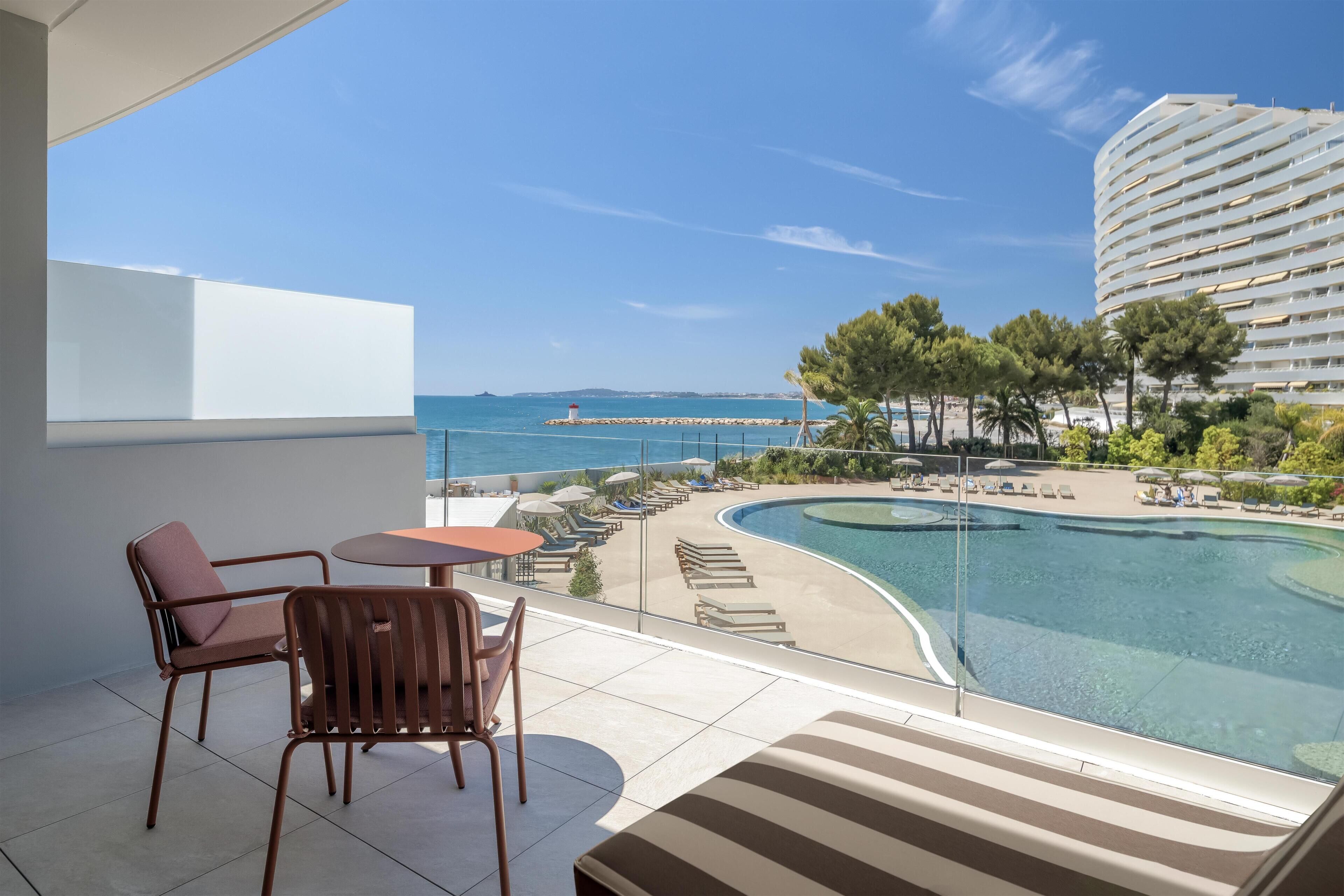 A balcony with a view of a swimming pool and a distant lighthouse.