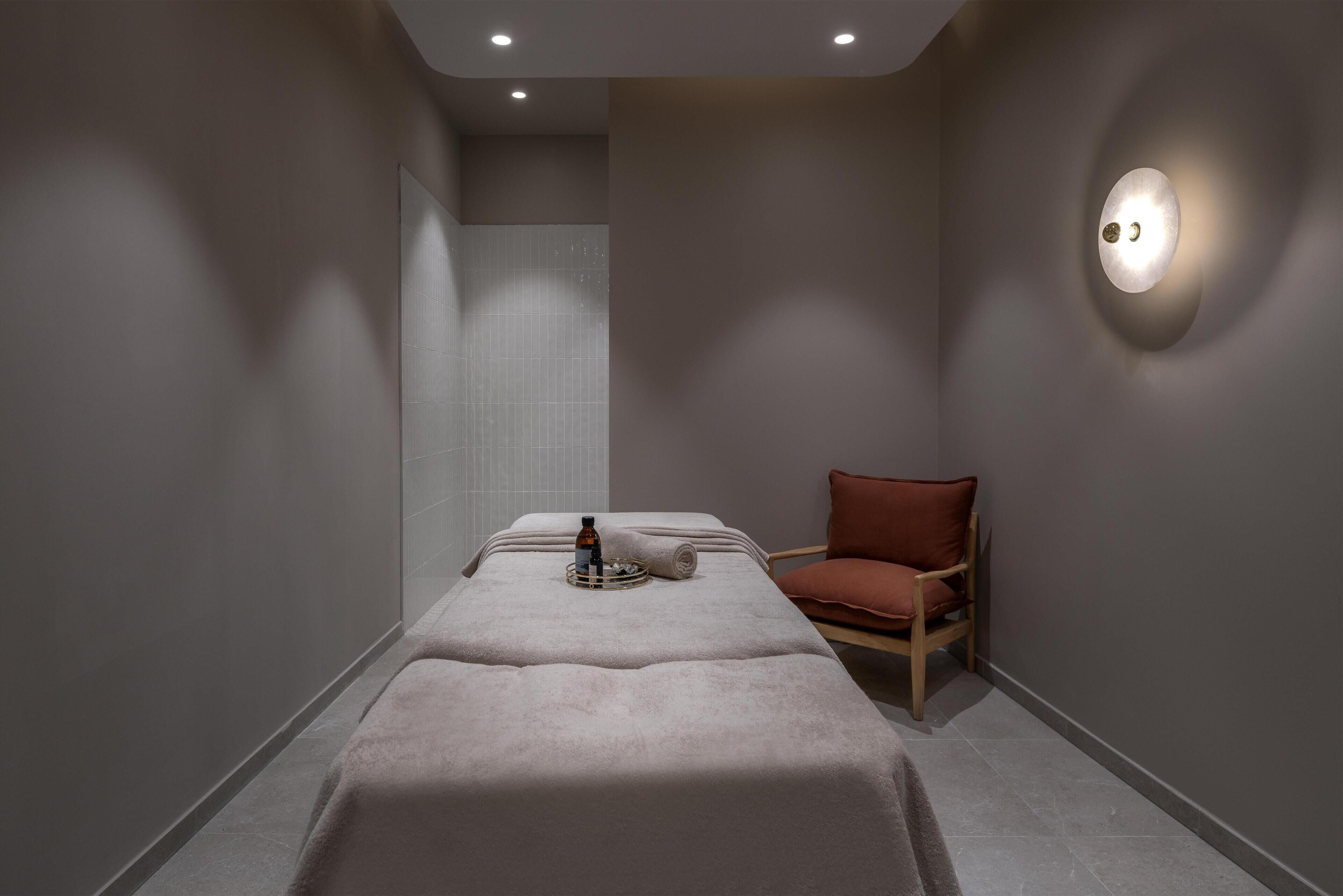 A spa room with a massage table, a chair, and a wall-mounted light fixture.