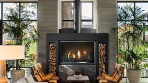 A modern living room with a fireplace, leather chairs, a sofa, and large windows with plants. - The Ava Hotel Paso Robles, Curio Collection By Hilton (Paso Robles)