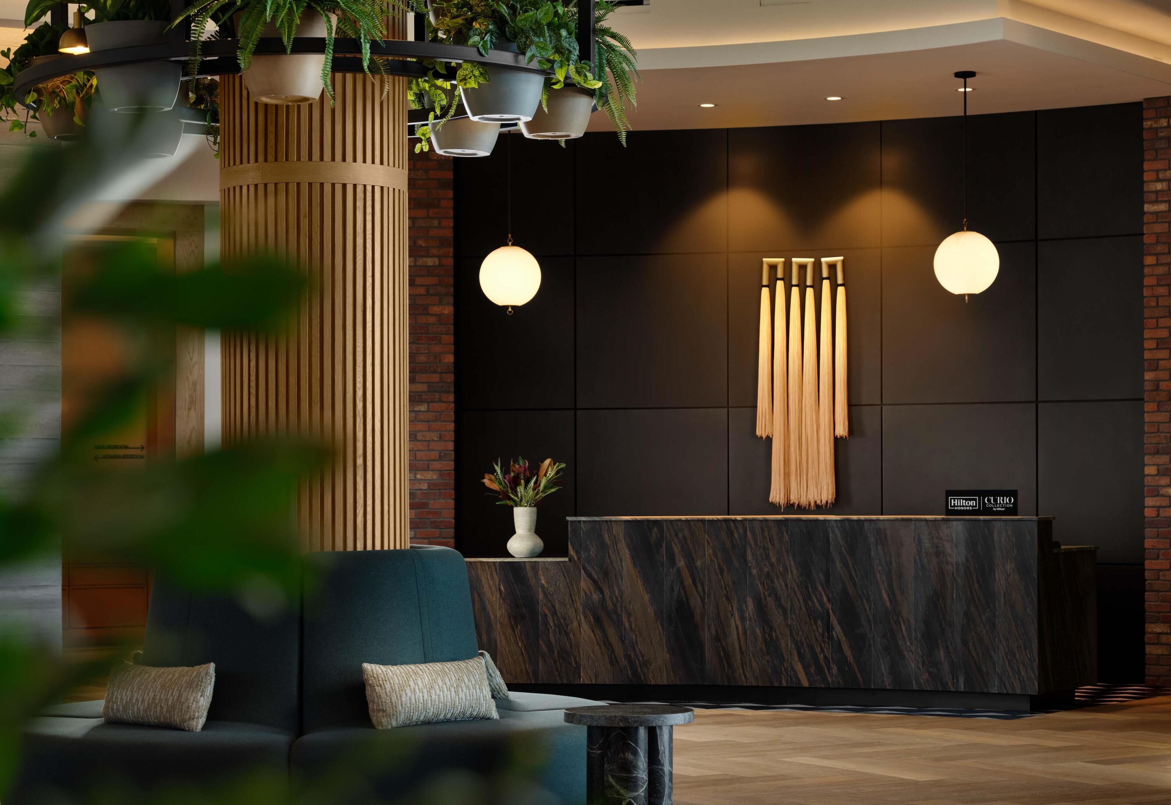 Un moderno vestíbulo de hotel con mostrador de recepción, zona de estar y plantas decorativas.
