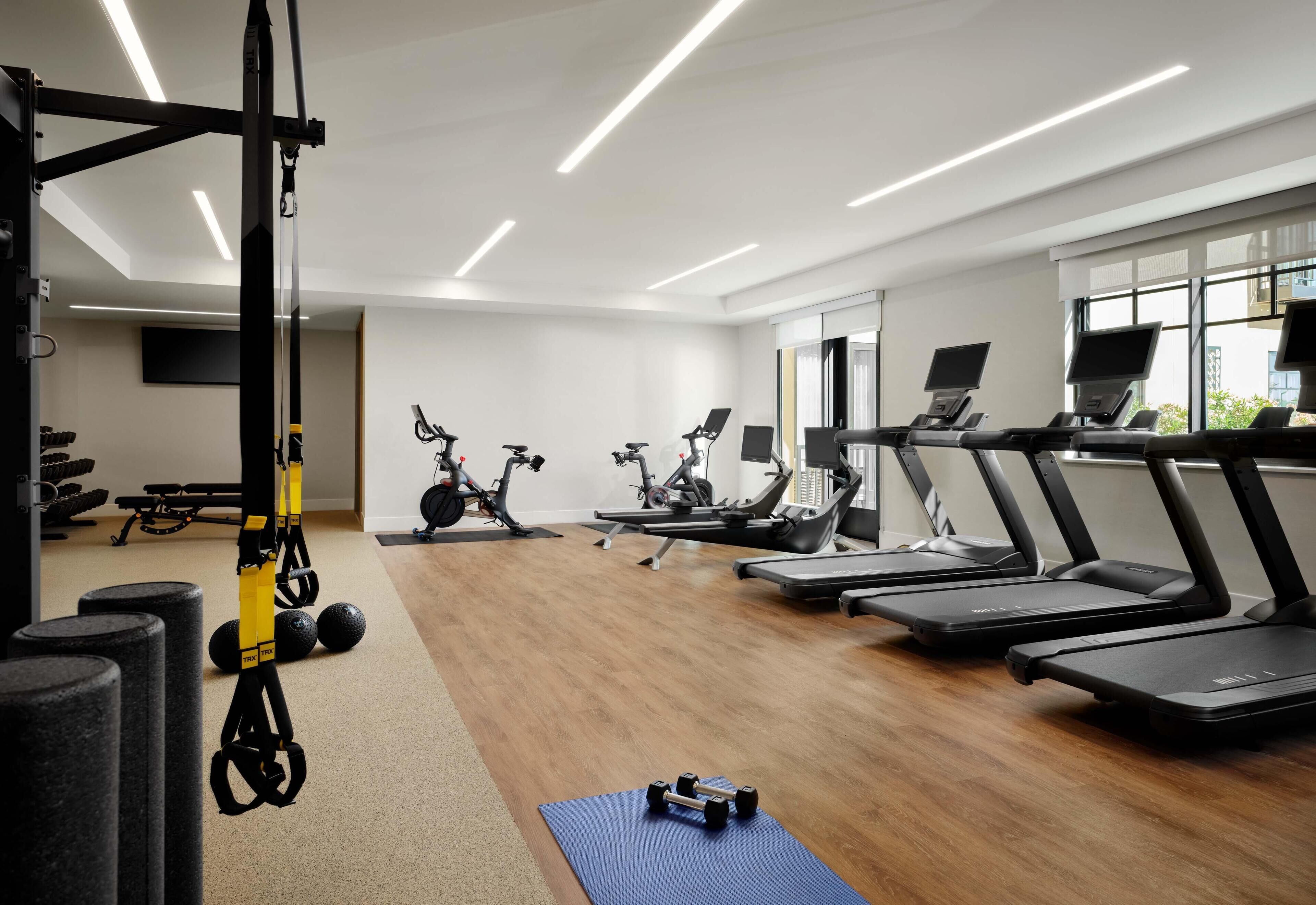 A modern gym with treadmills, elliptical machines, and free weights.