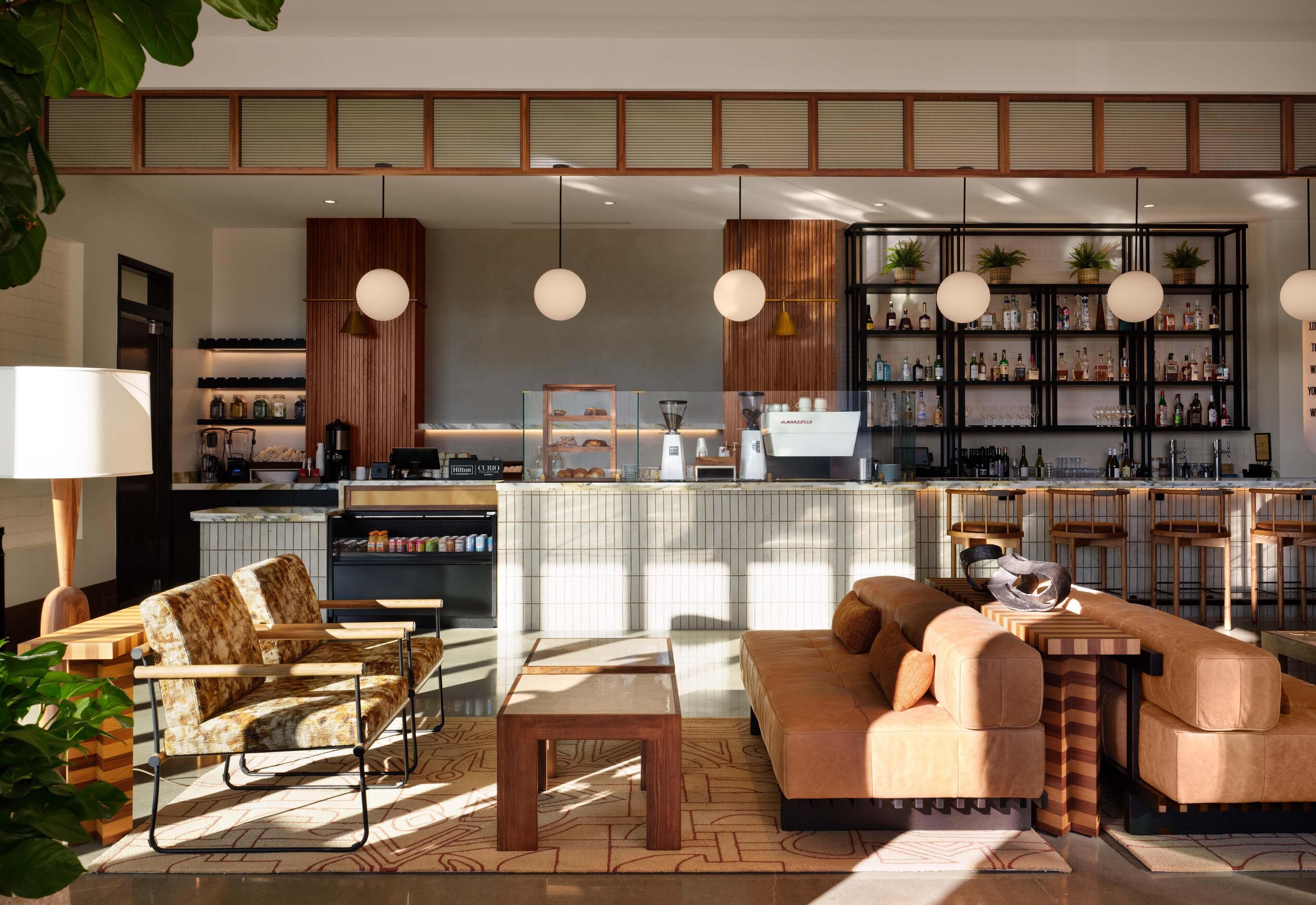 Una sala de estar moderna con sofá, sillas, una mesa de centro y una zona de cocina con barra y estanterías.