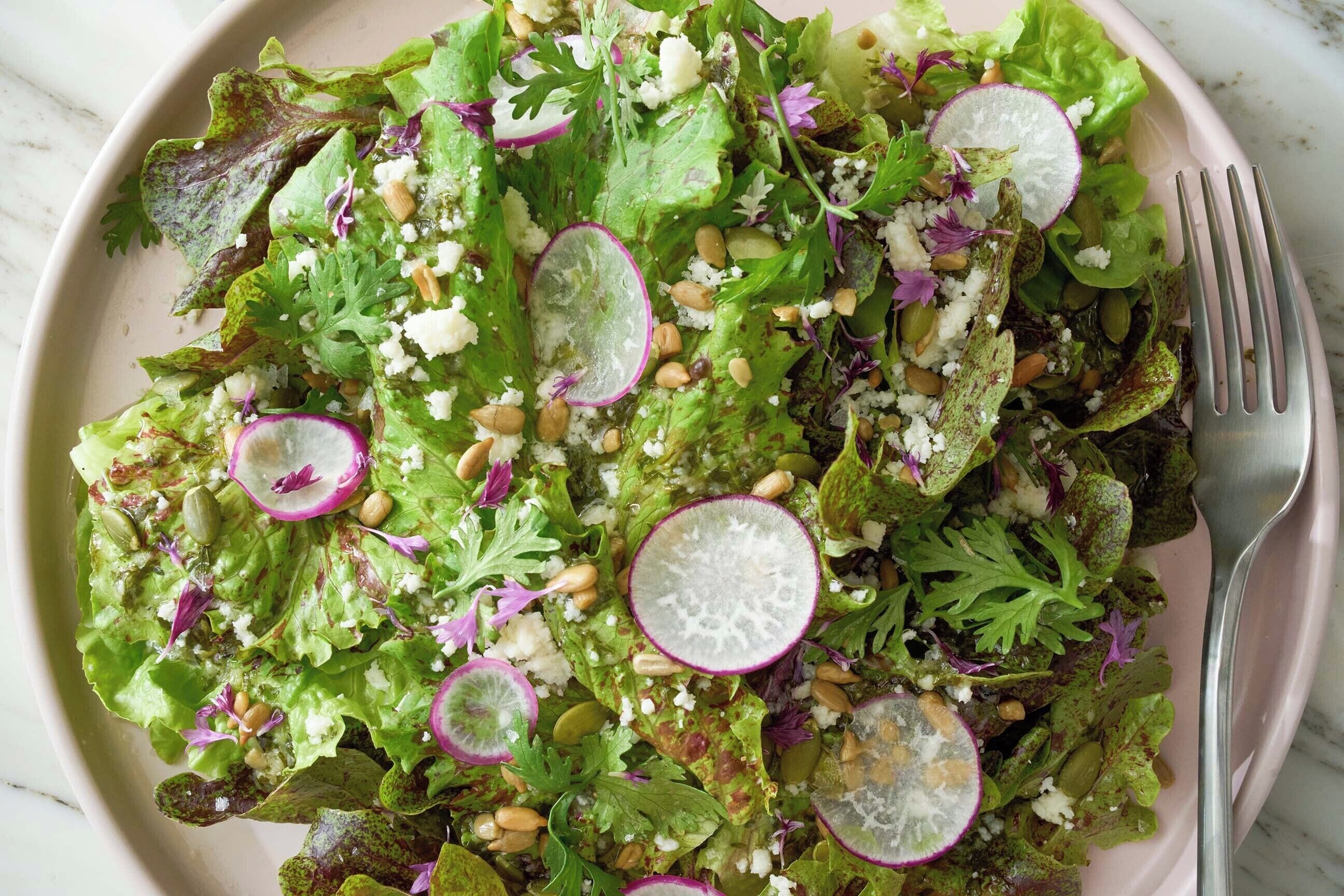 A plate of mixed greens salad with radish slices, nuts, and cheese.