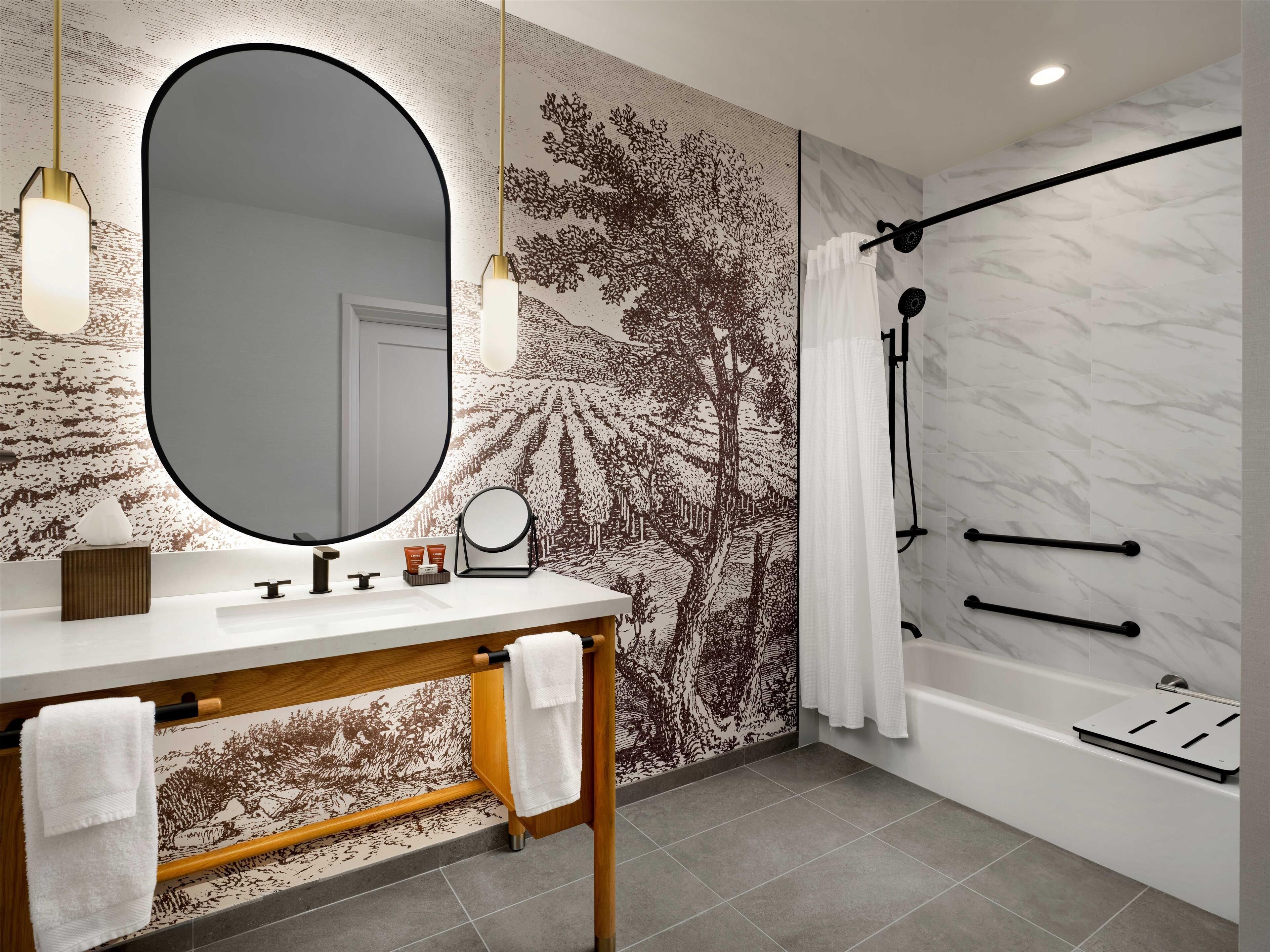Un baño moderno con un espejo ovalado grande, un tocador de madera, una bañera y una zona de ducha.