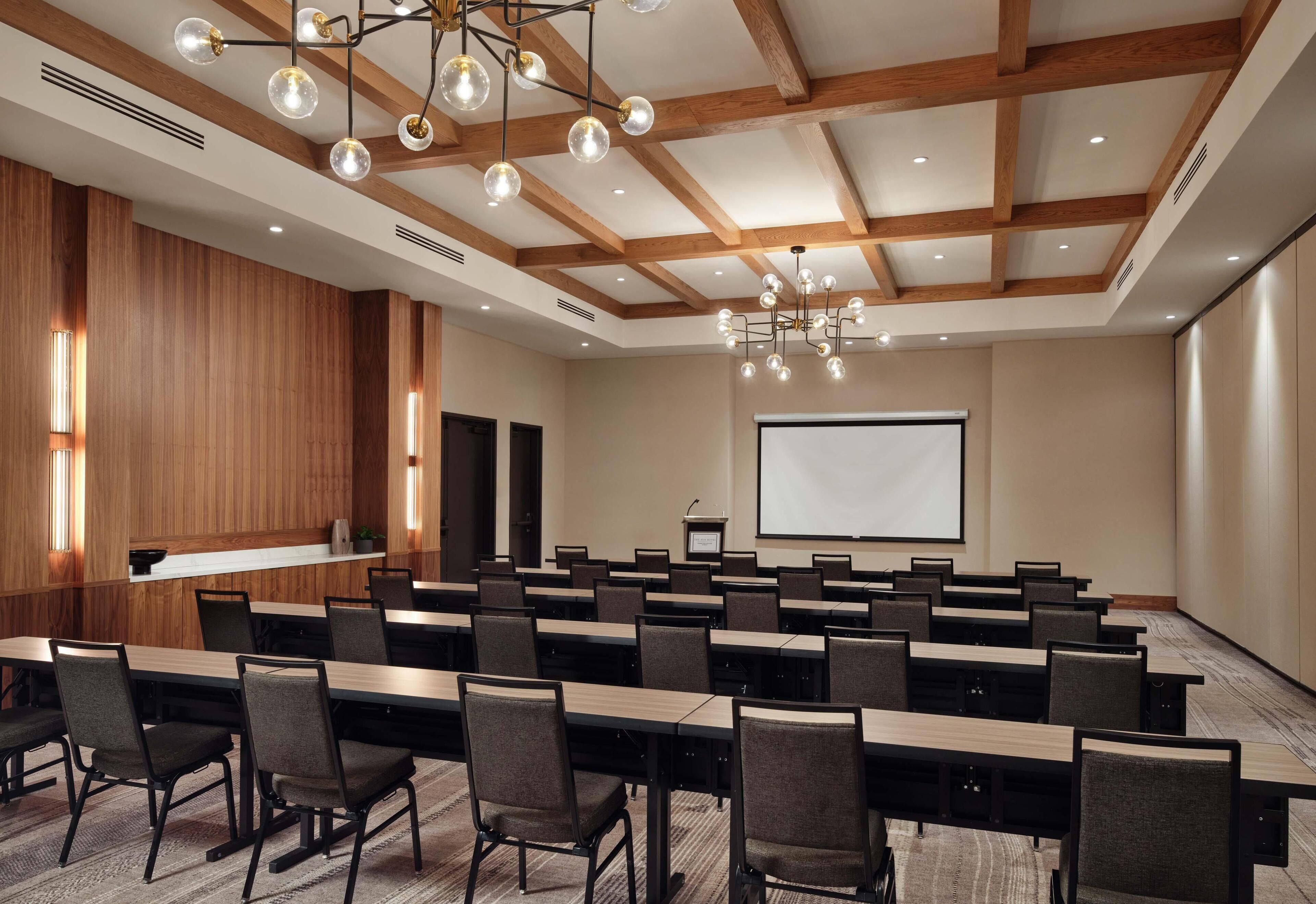 A conference room with long tables, chairs, a projector screen, and a wooden ceiling.