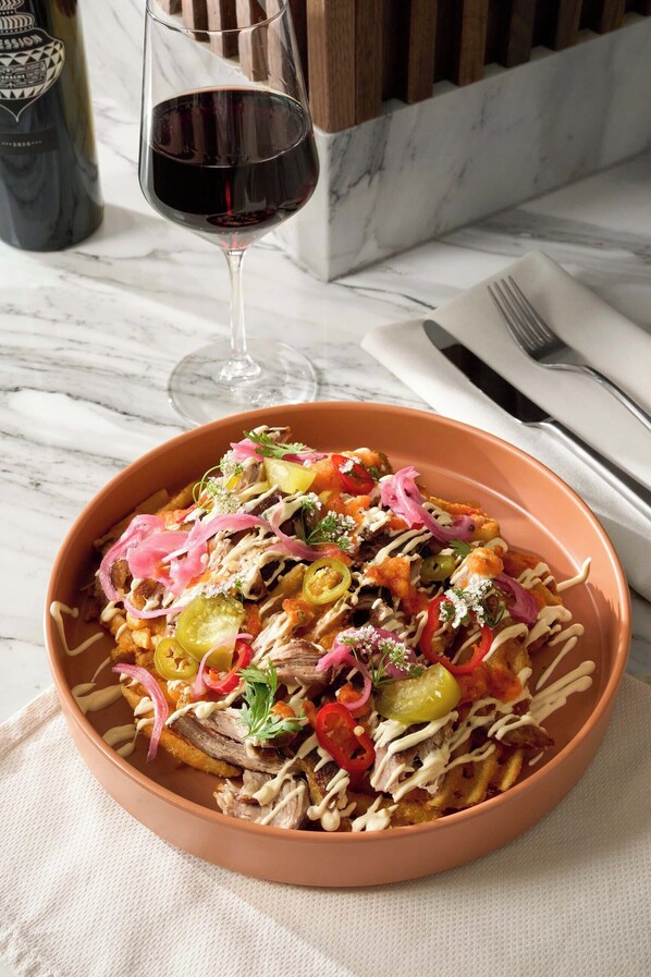 A bowl of nachos topped with various ingredients and a glass of red wine. - The Ava Hotel Paso Robles, Curio Collection By Hilton (Paso Robles)