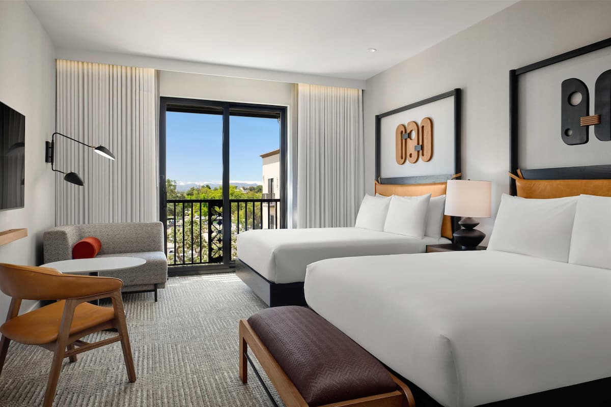 A hotel room with two beds, a sofa, a chair, a bench, a TV, and a balcony with a view.