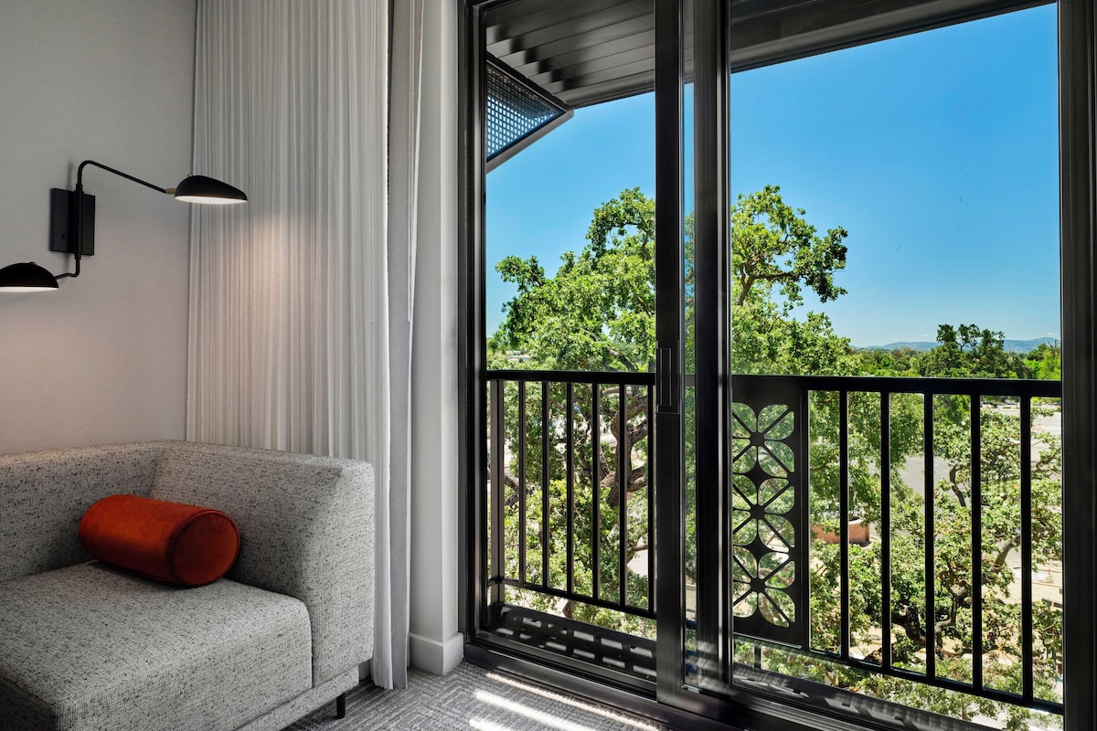 A modern room with a grey sofa, a red cushion, and a large window with a black metal railing.